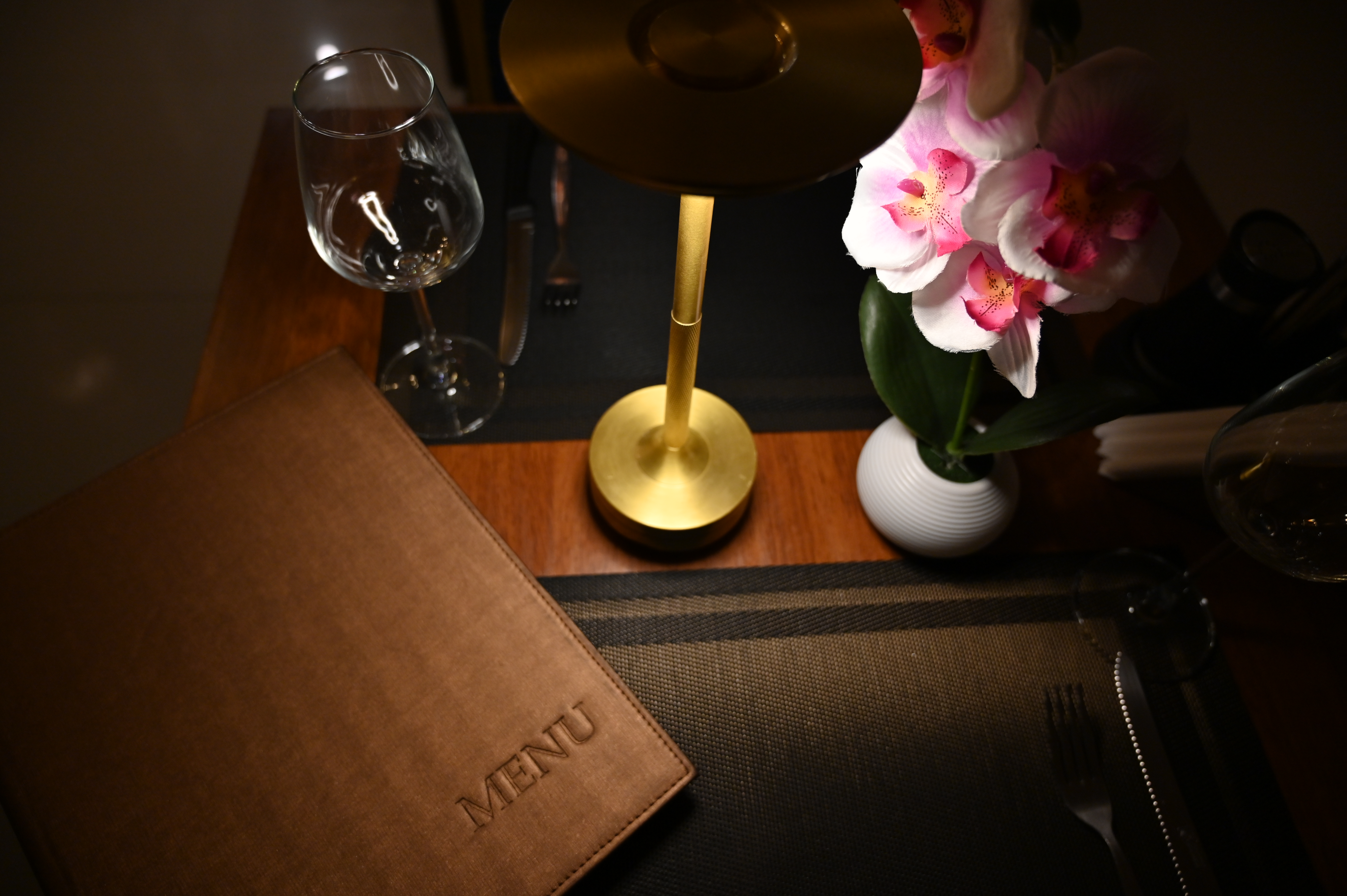 A closed leather menu on a candlelit table set for two, seen from above