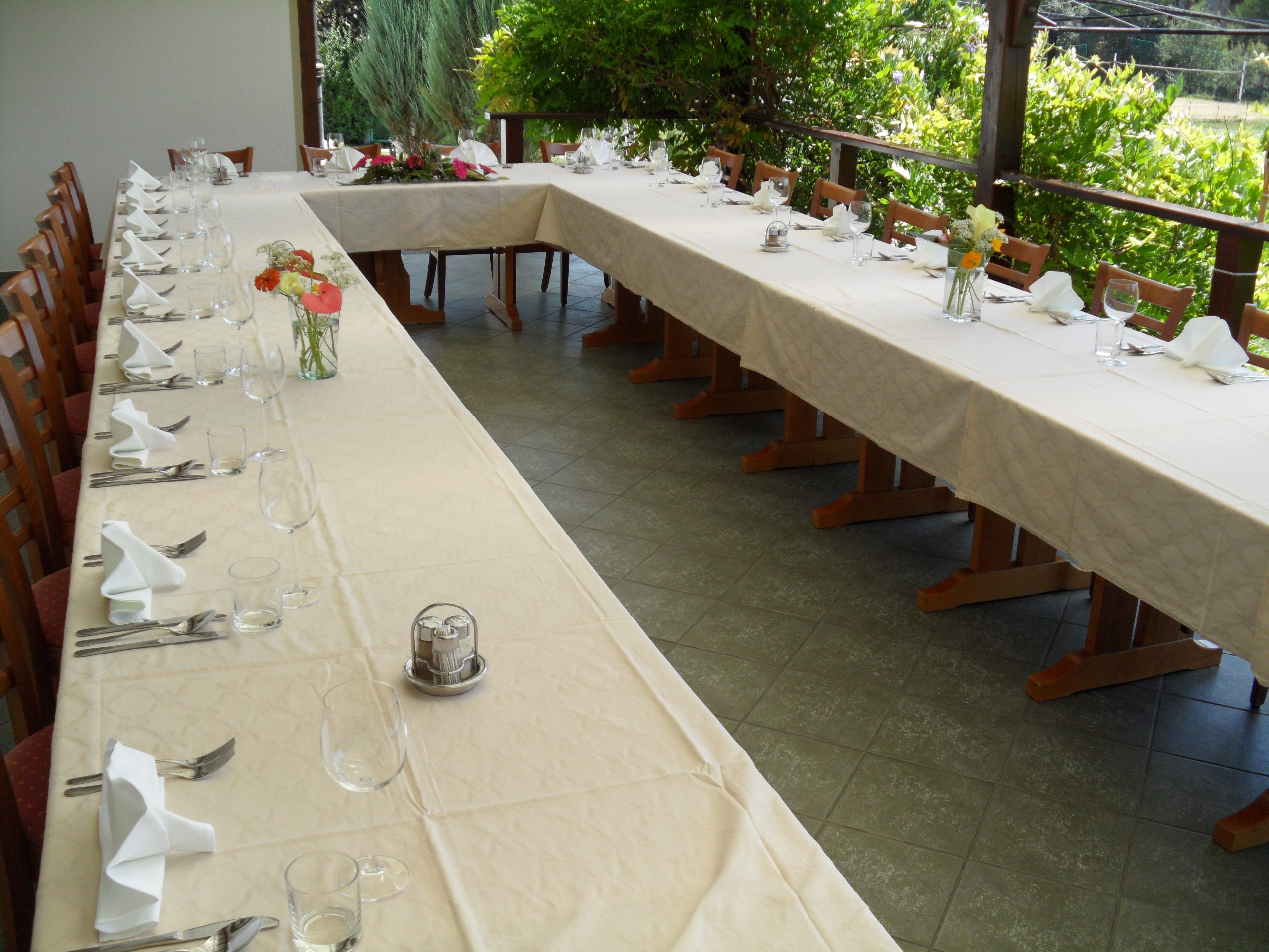 Long tables joined in a U shape and laid with white cloths, glasses and folded napkins for a large group