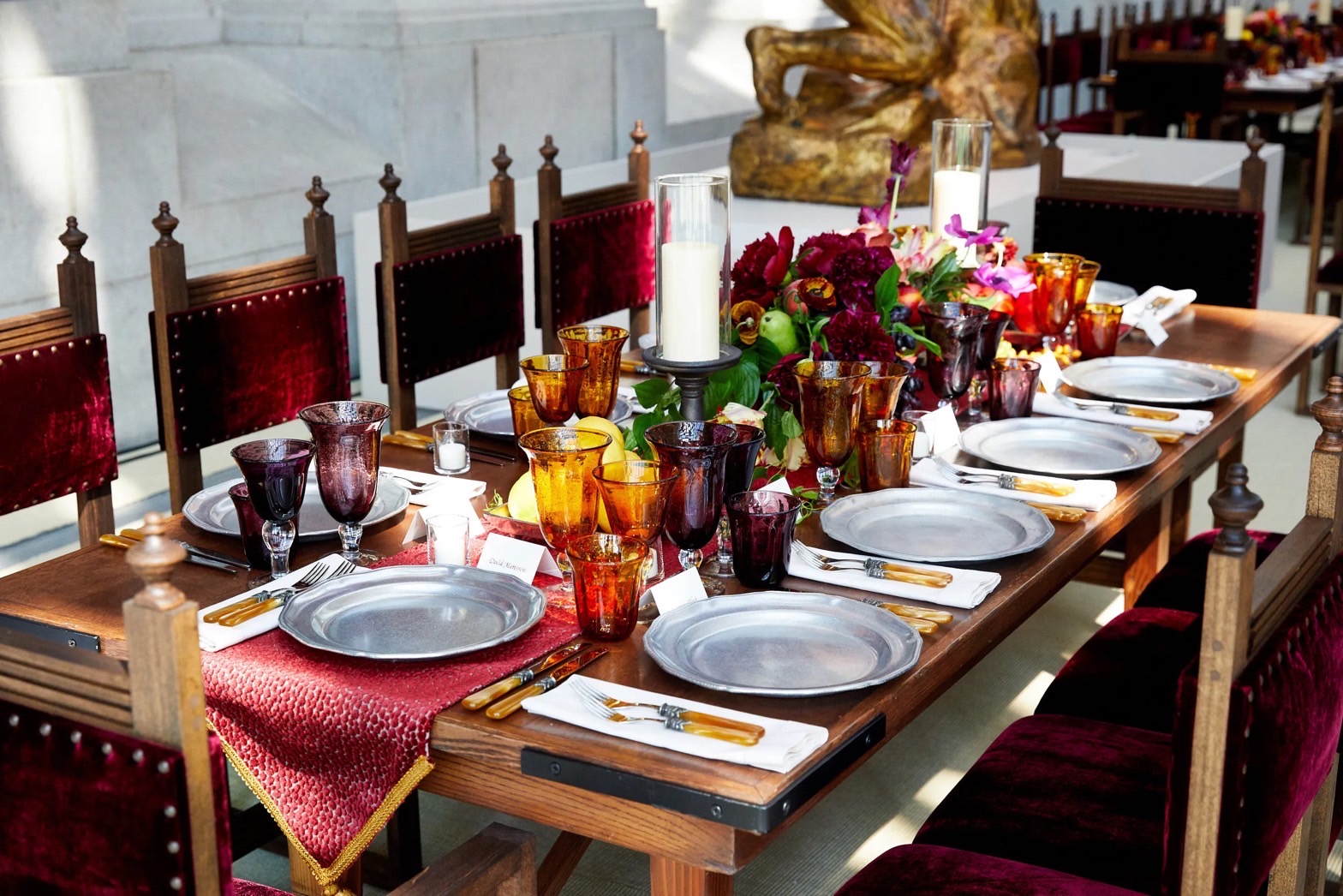 A long wooden table laid for ten with pewter plates, amber glasses, candles and flowers