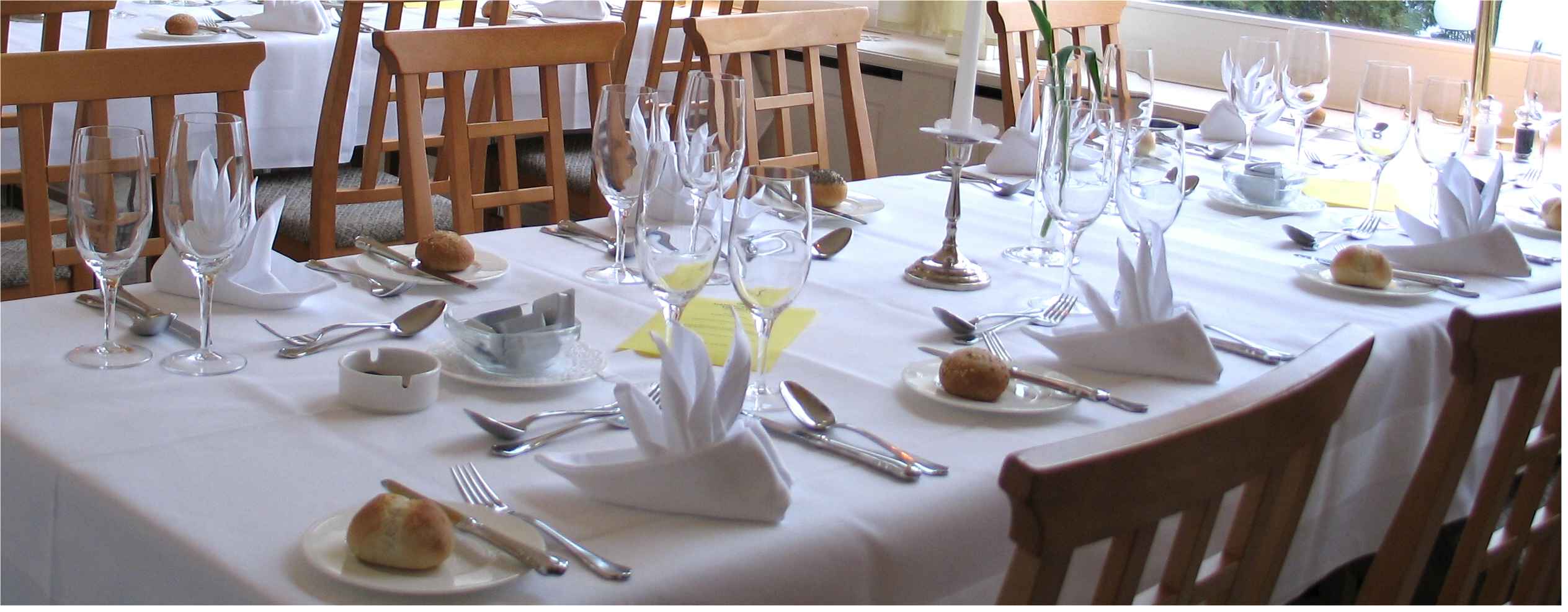 A long restaurant table laid with folded napkins, bread rolls, glasses and cutlery for a group meal