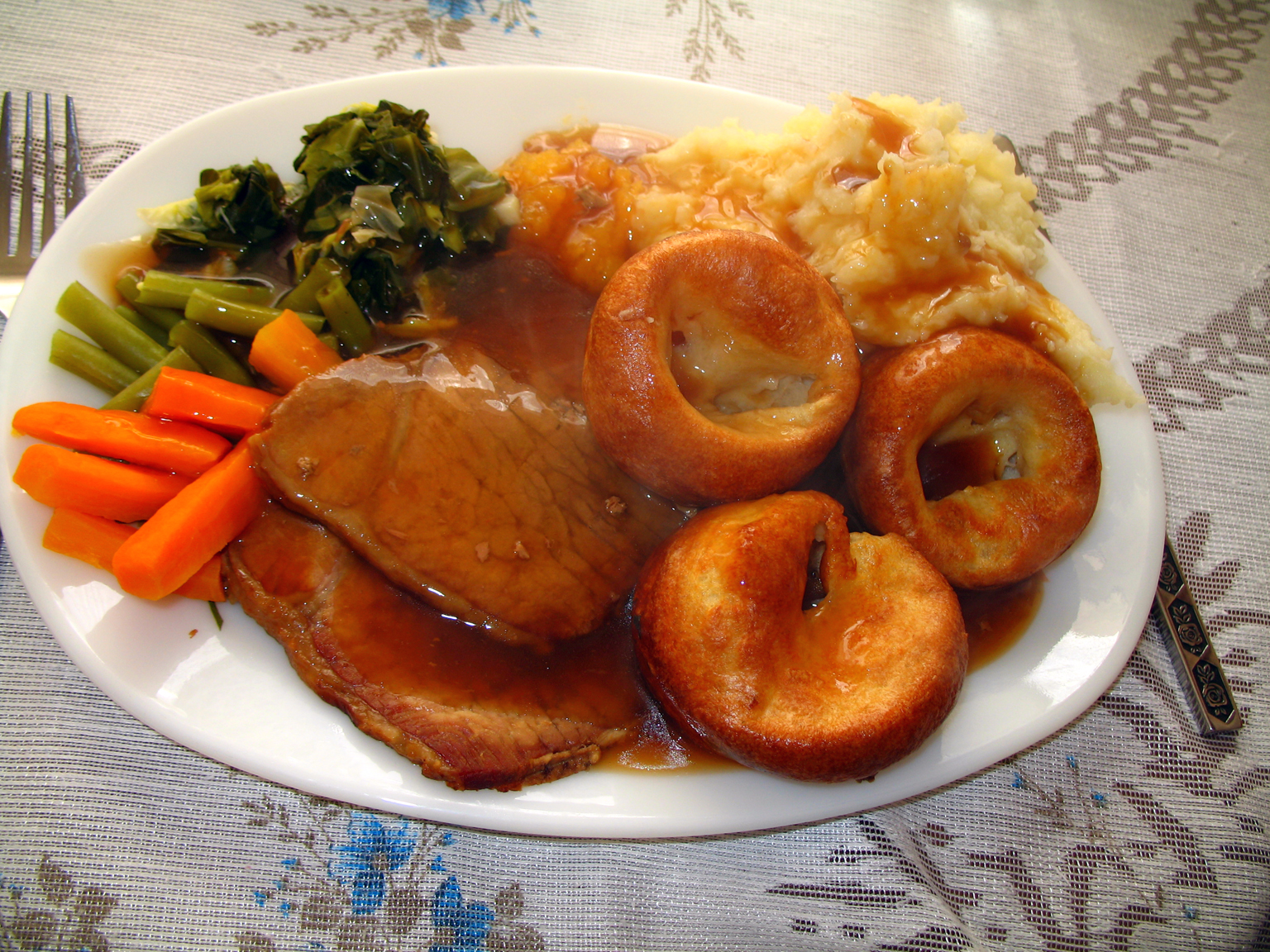 A plate of roast beef, Yorkshire puddings, mashed potato, carrots and greens on a lace tablecloth at home
