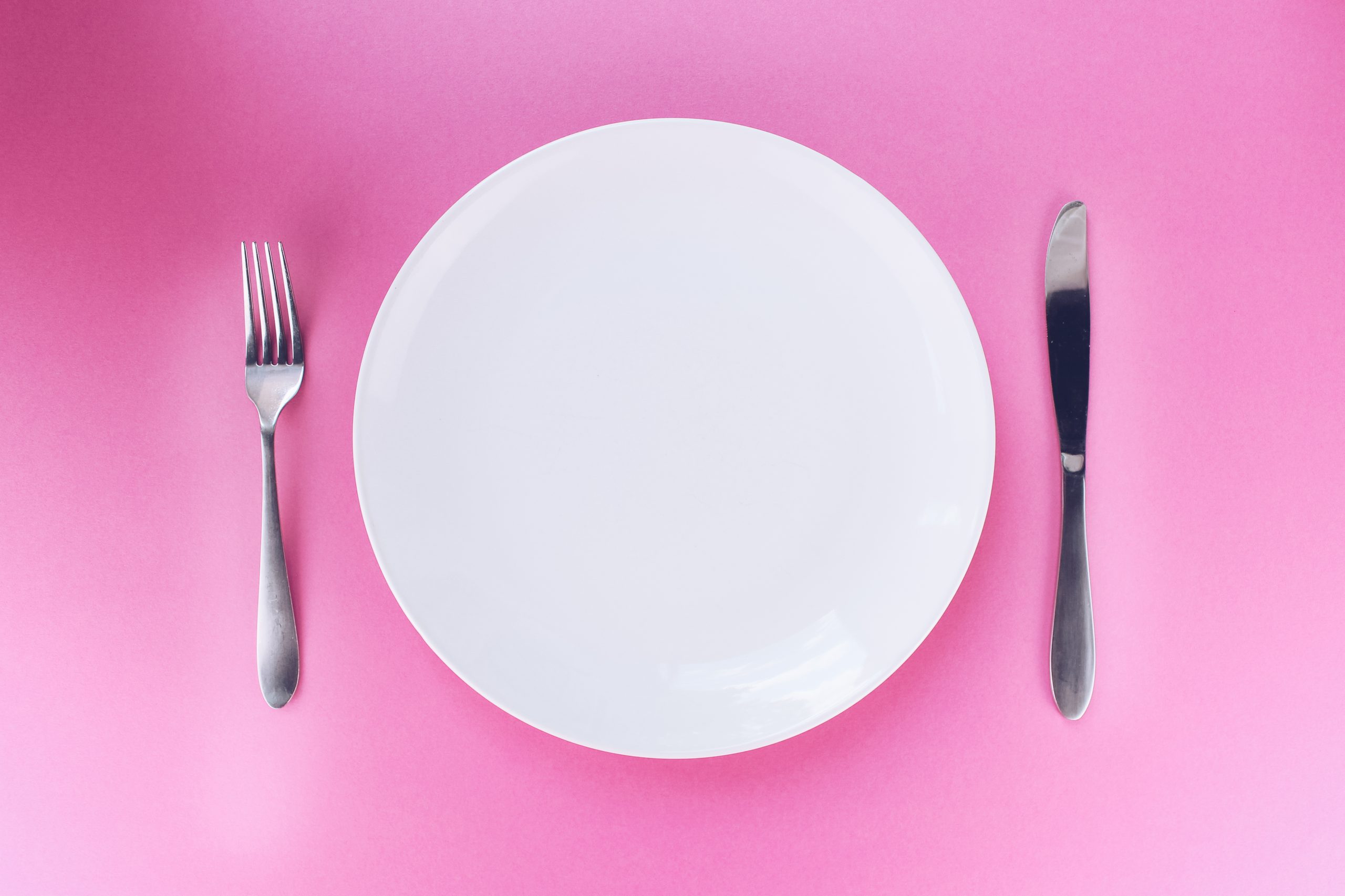A white plate with a fork on the left and a knife on the right on a pink background