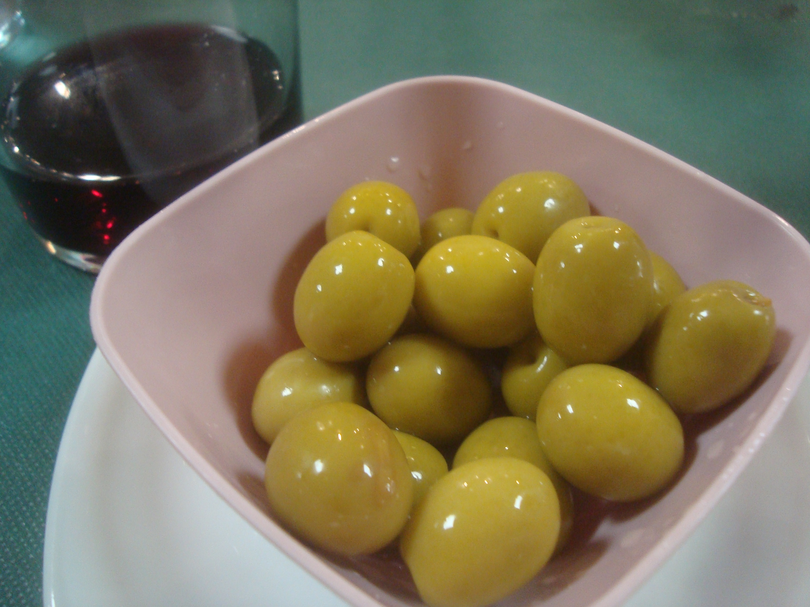 A small bowl of green olives beside a glass of red wine on a restaurant table