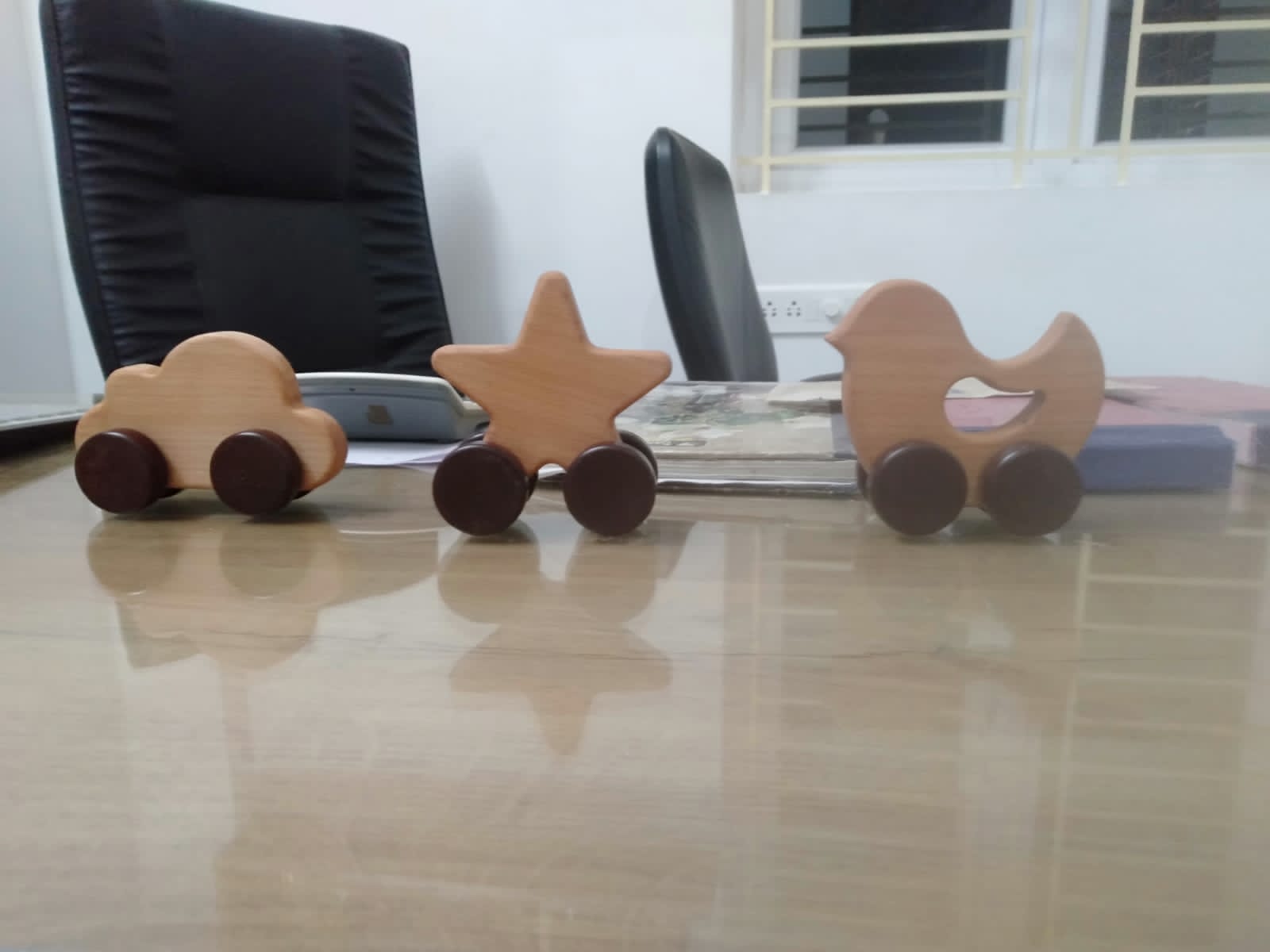 Three small wooden push-along toys shaped like a car, a star and a bird on a polished table