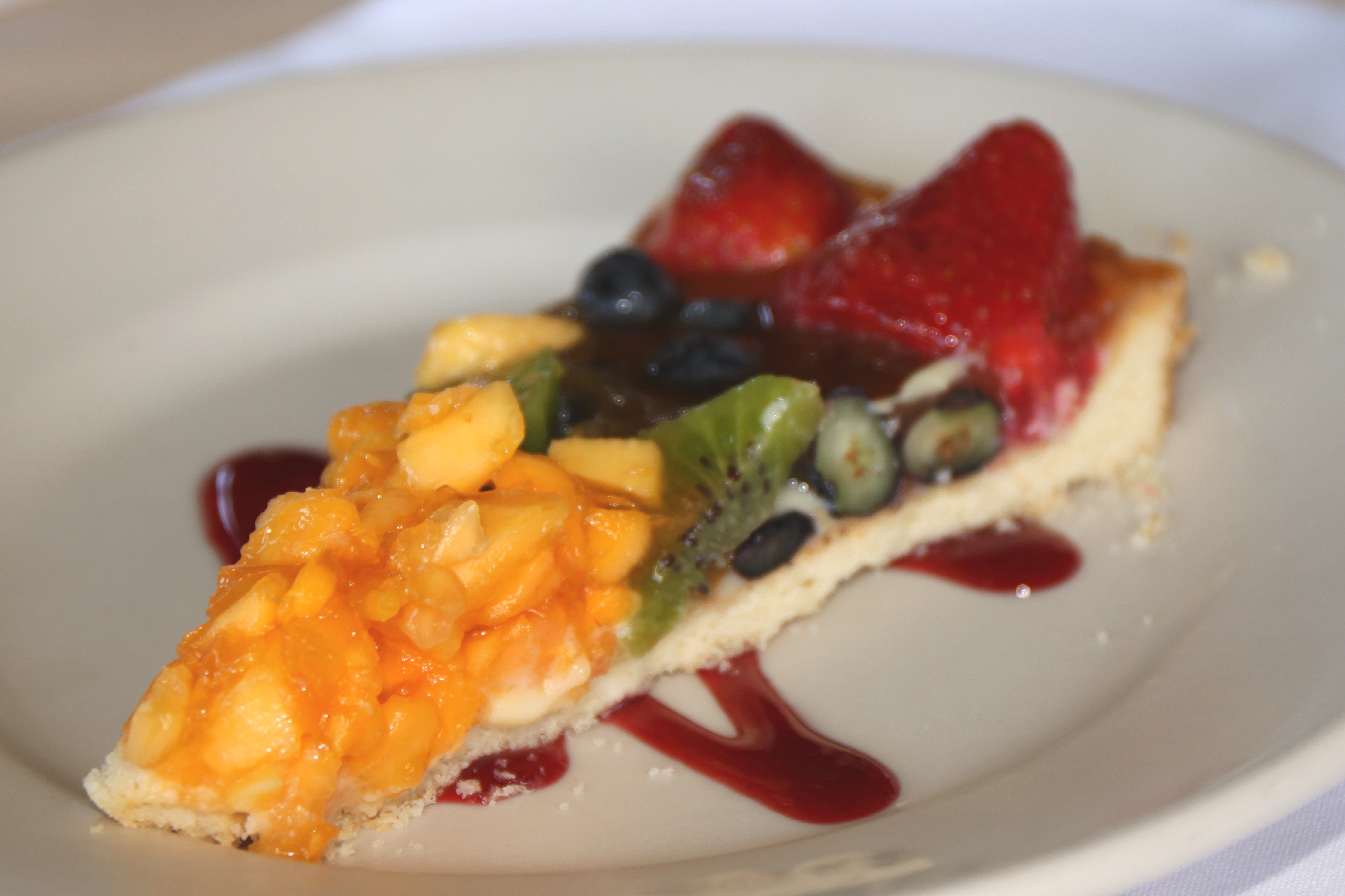 Slice of fruit tart with strawberries, kiwi and mango on a white plate