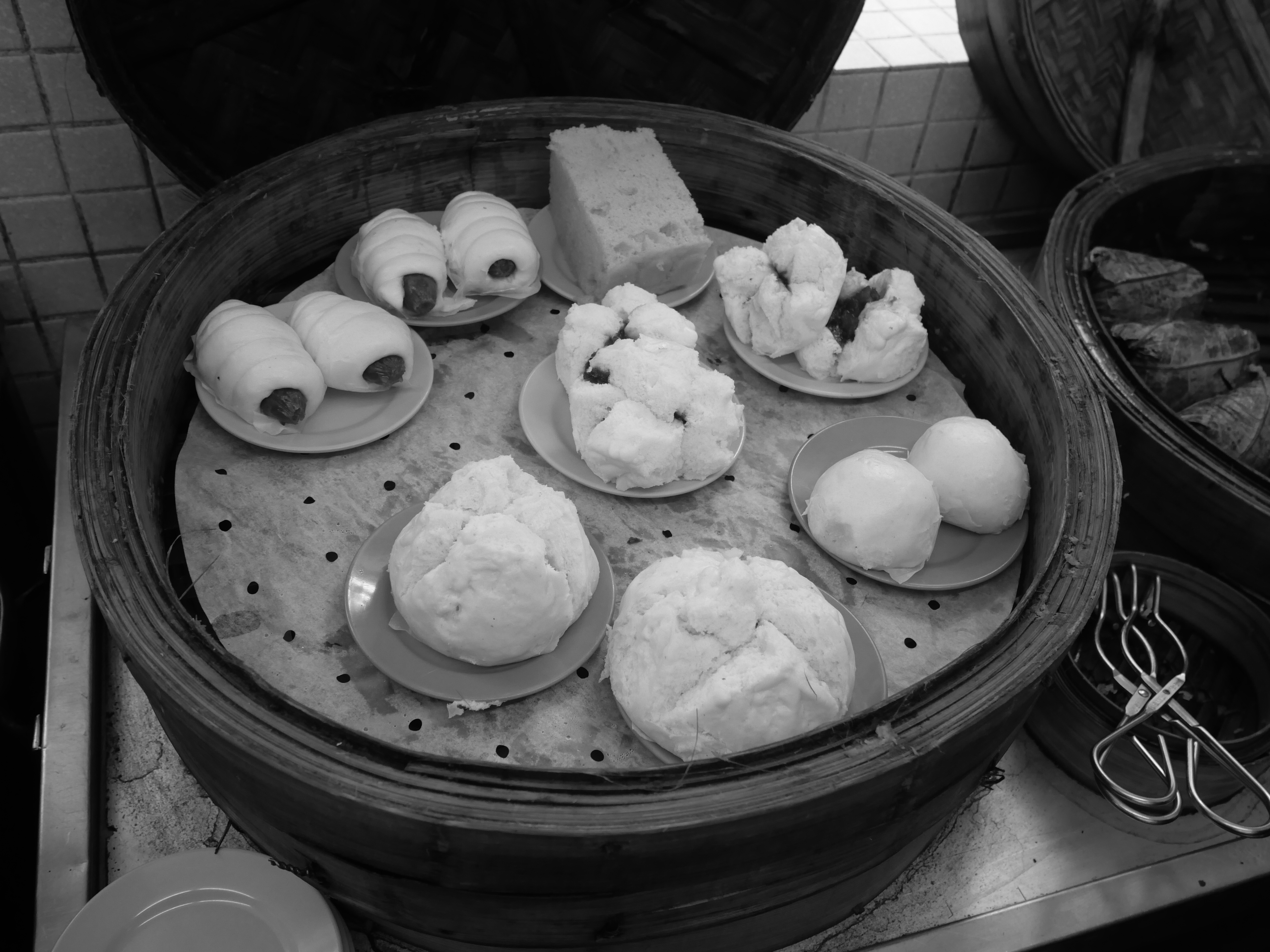 Bamboo steamer filled with small plates of steamed buns and dumplings, black and white