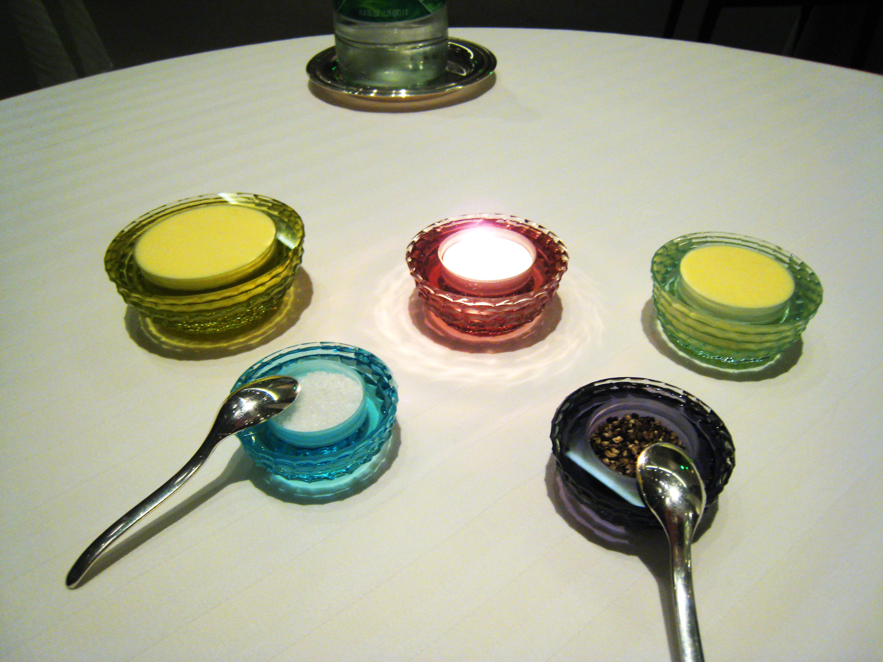 Tealight glowing among small glass dishes of butter, salt and pepper on a white tablecloth