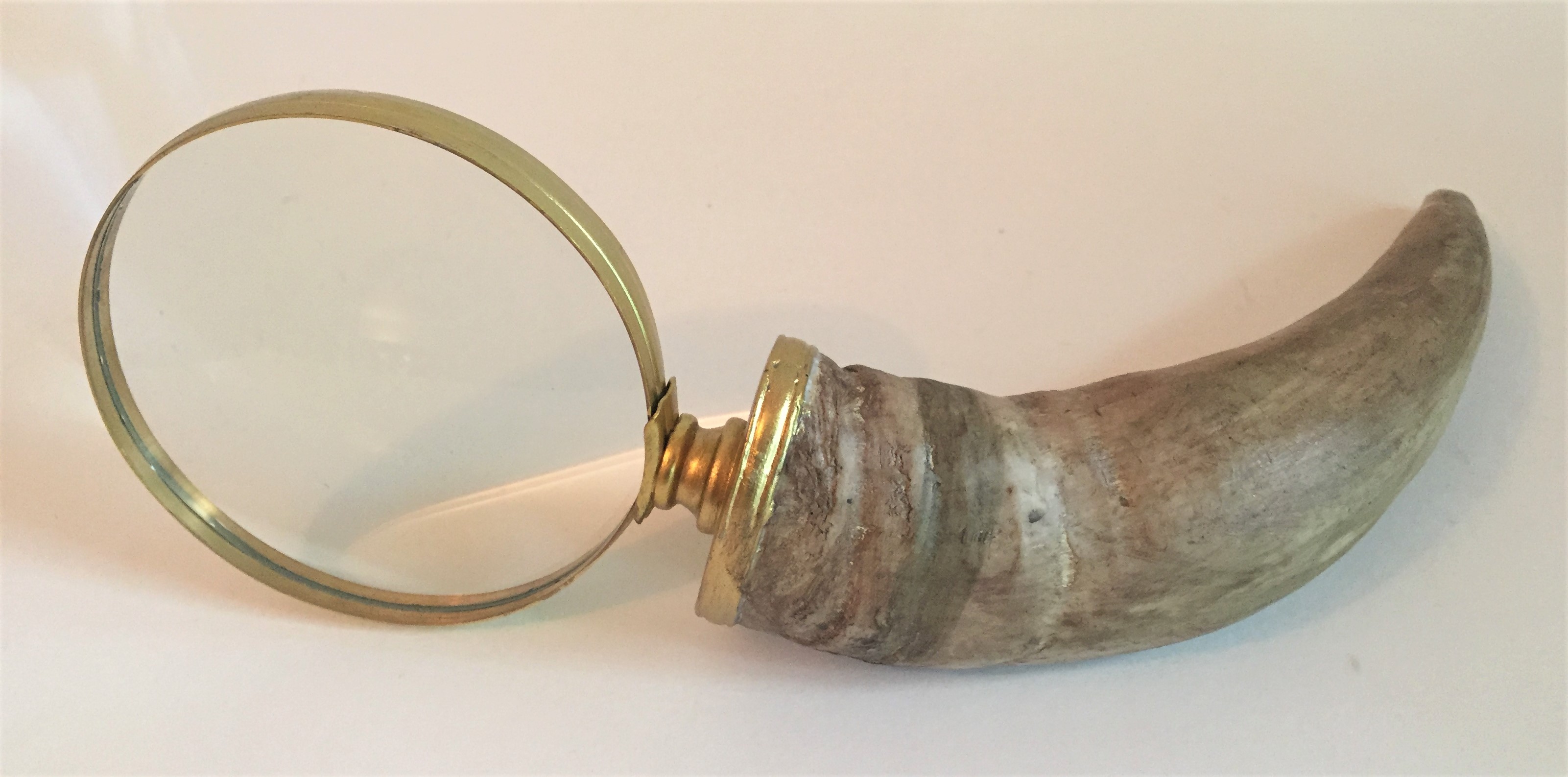 Brass magnifying glass with a curved horn handle on a white surface