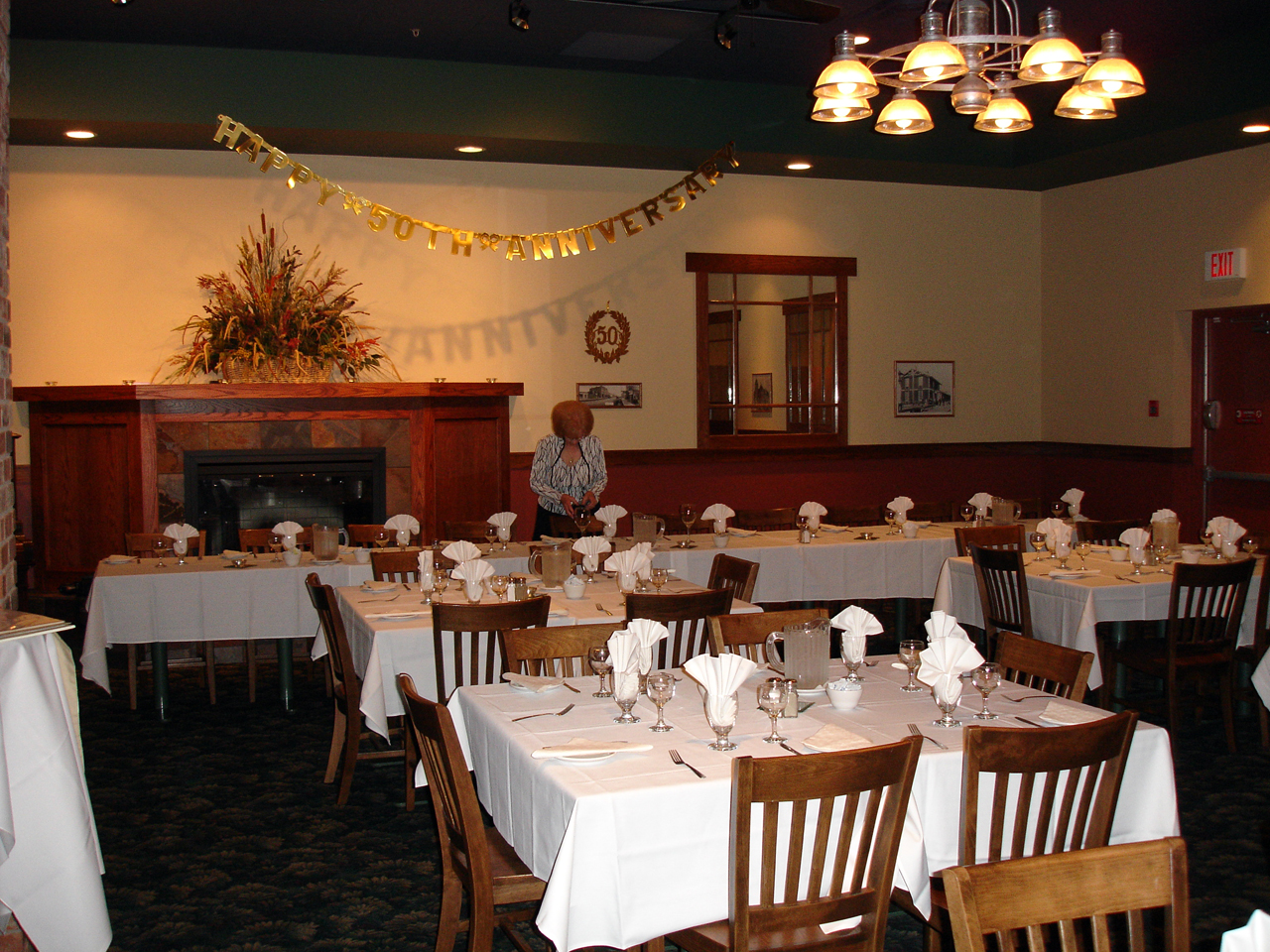 A function room with several tables laid in white linen and folded napkins, decorated for an anniversary dinner