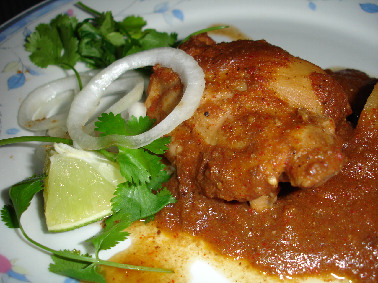 Spiced chicken curry served with a lime wedge, onion rings and coriander on a floral plate