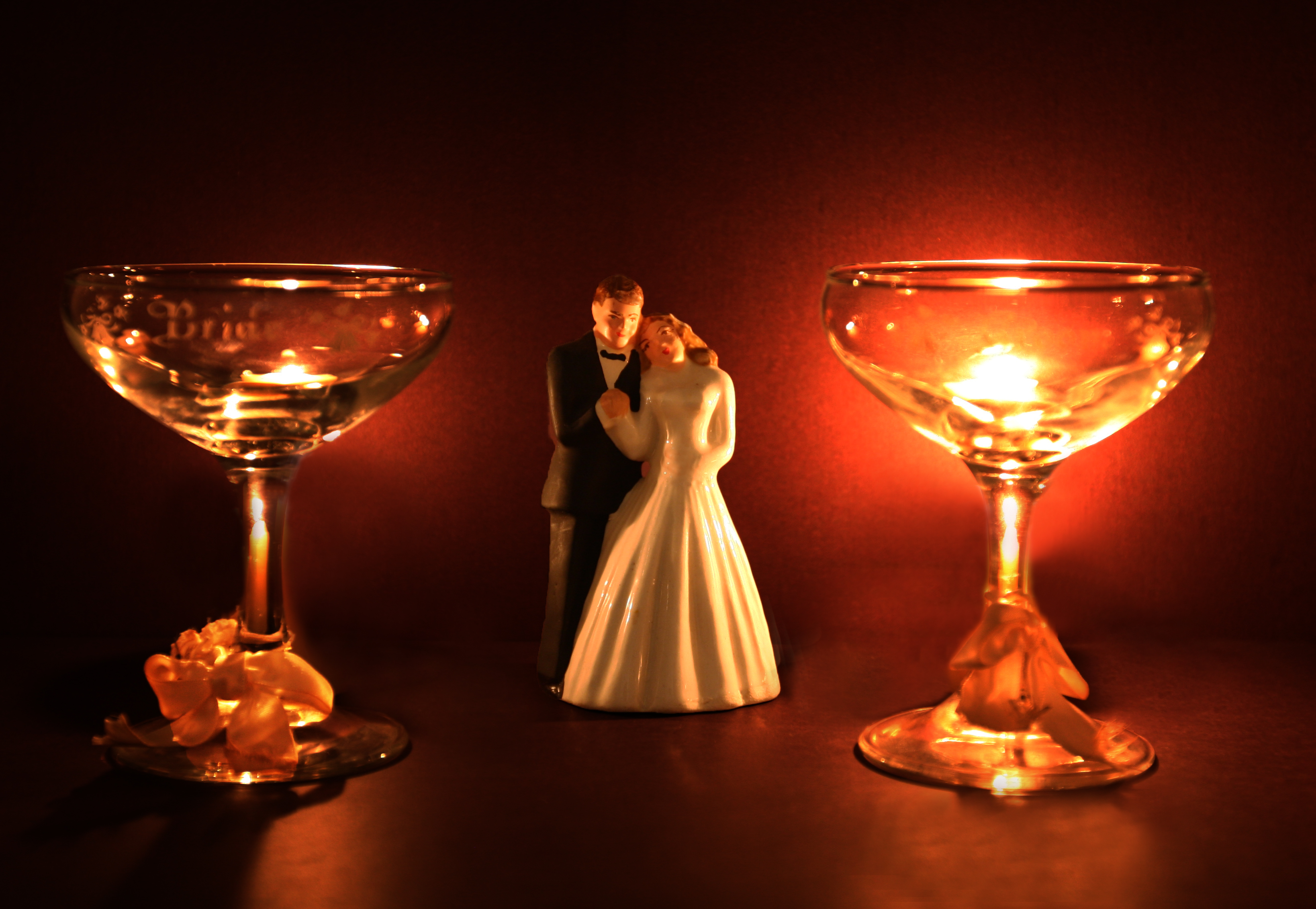 Two etched coupe glasses lit warmly either side of a small wedding couple figurine