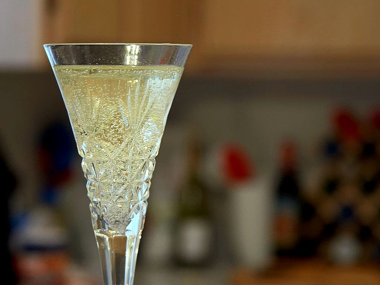 Cut-crystal flute of sparkling wine with bubbles rising, blurred room behind