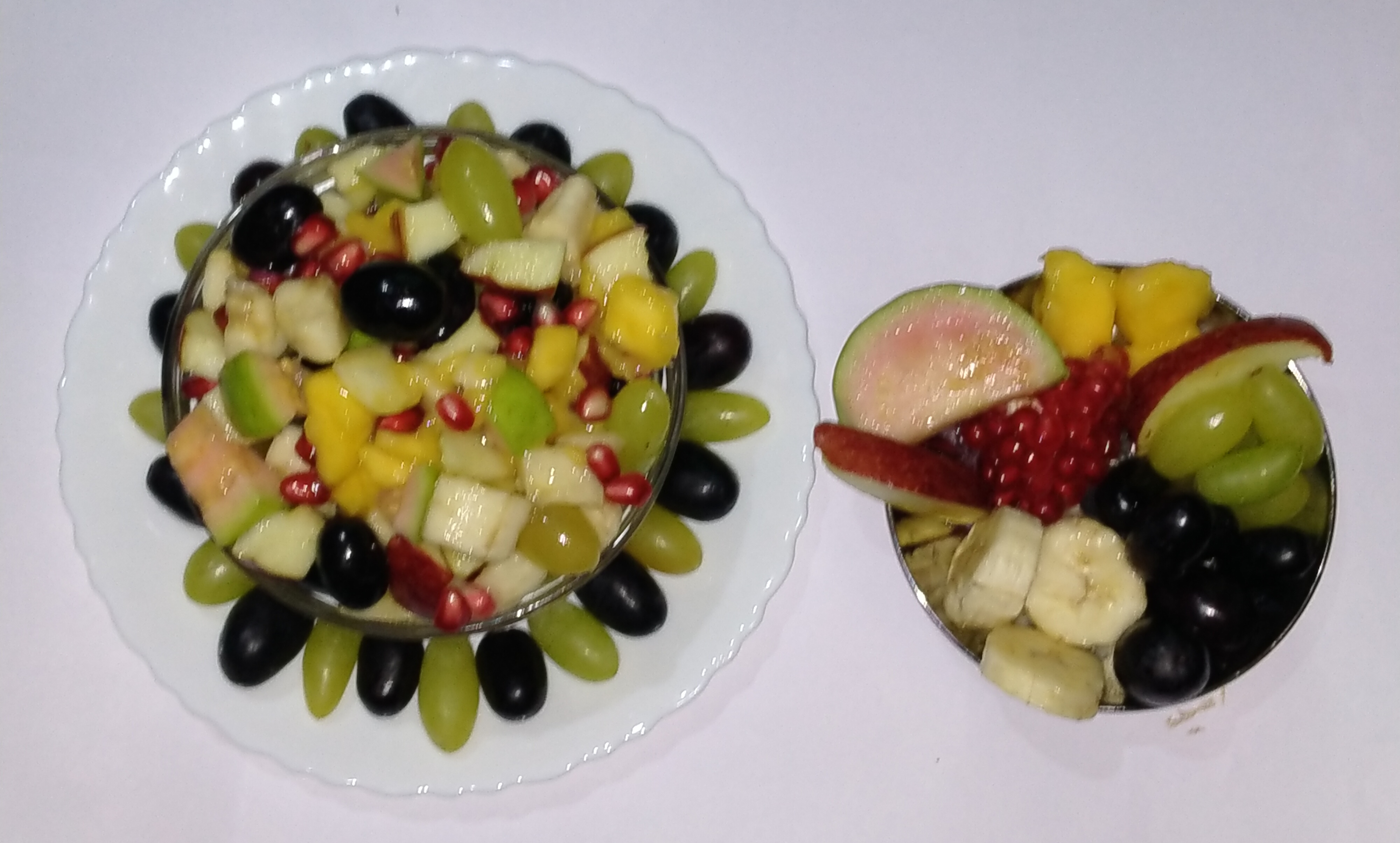 Two bowls of chopped fresh fruit with grapes, pomegranate seeds and banana