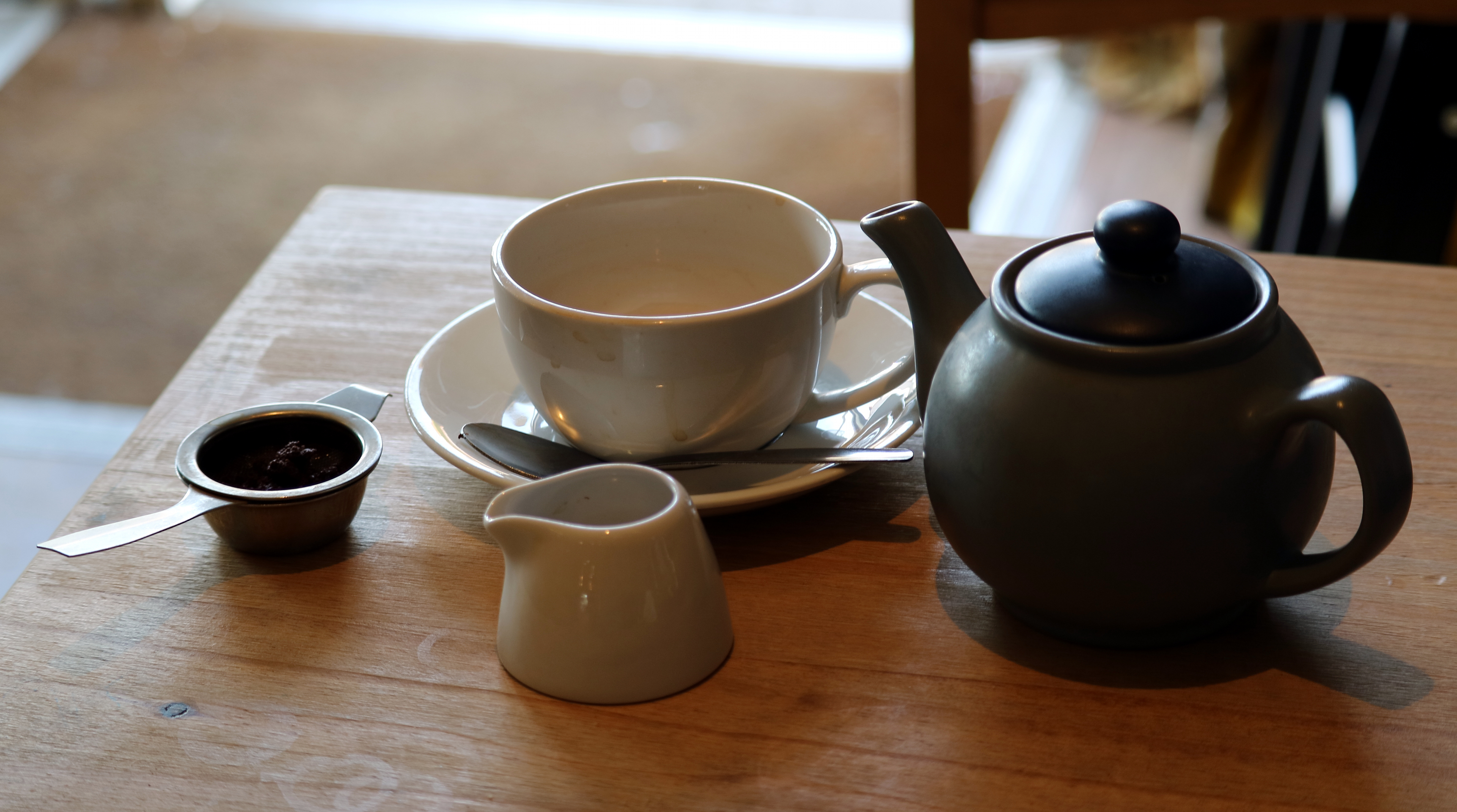 A teapot, cup and saucer and small milk jug on a wooden café table